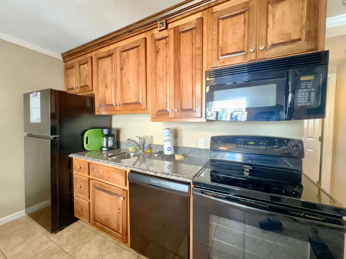 A cozy kitchen with wooden cabinets, a granite countertop, black appliances, and a kitchen sink. The layout is open and functional, making it easy for multiple people to participate in meal preparation.