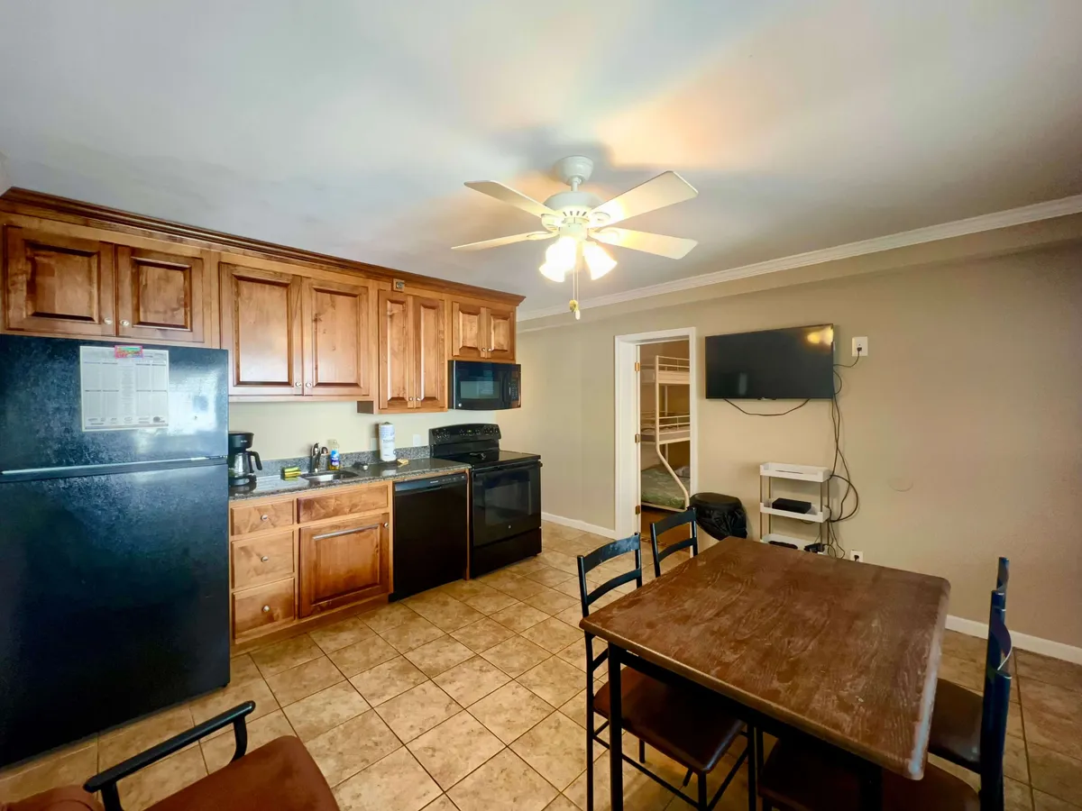A bright and homely kitchen scene featuring kitchen cabinets, modern appliances, and a dining table set for family meals. The countertops are clear, and the space looks inviting for both cooking and socializing.