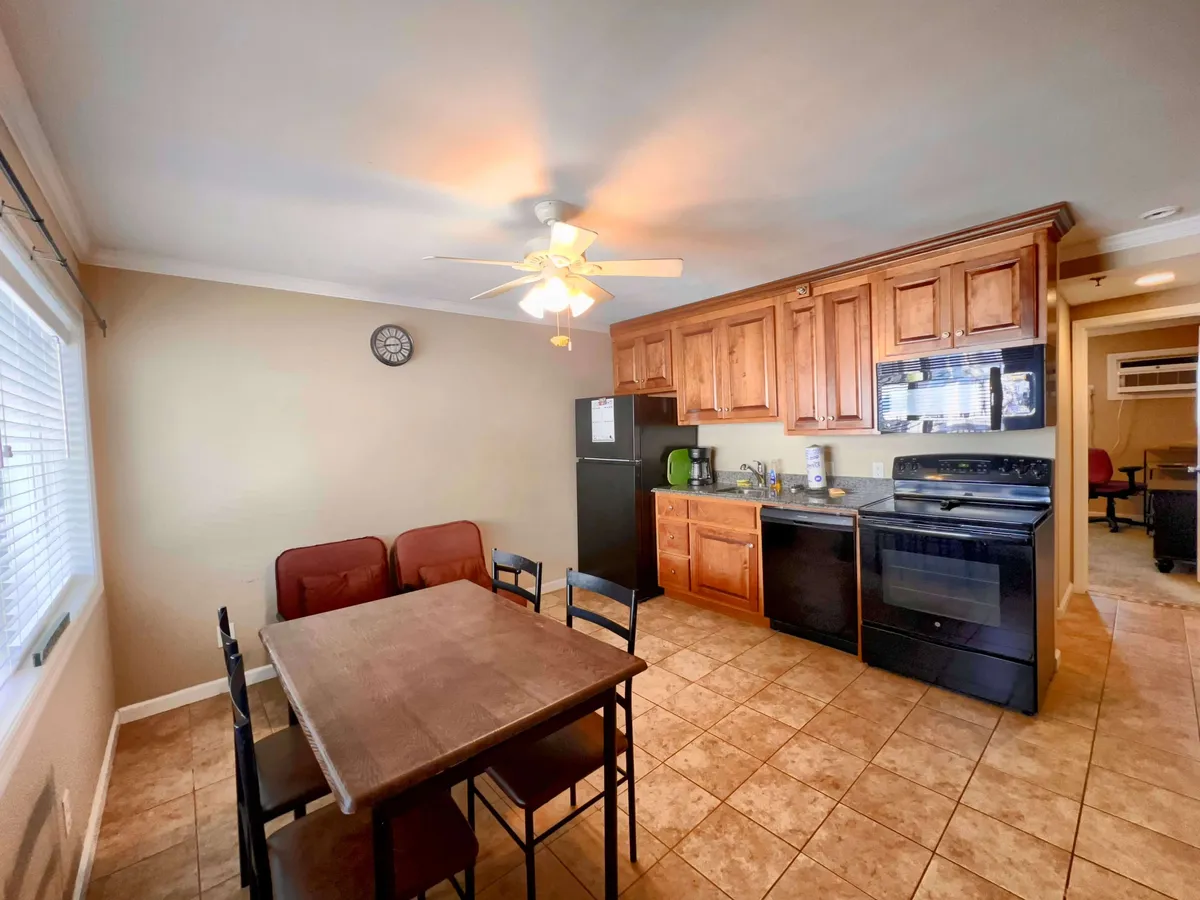 A welcoming interior shot featuring a dining table adjacent to the kitchen, with kitchen appliances and a clock visible. The window allows in natural light, making the atmosphere cozy and inviting for shared meals.
