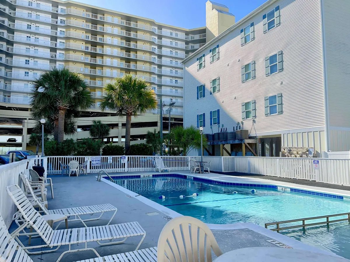 This image showcases the inviting swimming pool area surrounded by lounge chairs and palm trees, with buildings in the background. The bright, open space is perfect for morning coffee, sunbathing, or group gatherings under the sun.