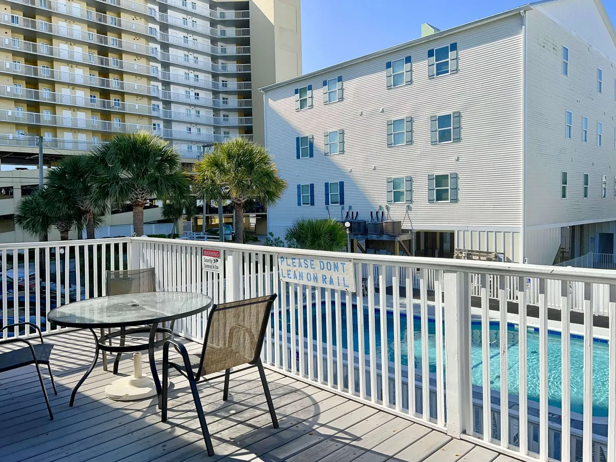 An outdoor dining table is set next to the swimming pool, with palm trees swaying overhead. The scene captures guests enjoying meals, lounging in the sun, and socializing in a casual, cheerful environment. The pool and dining area together emphasize both relaxation and the opportunity to enjoy shared experiences outdoors.