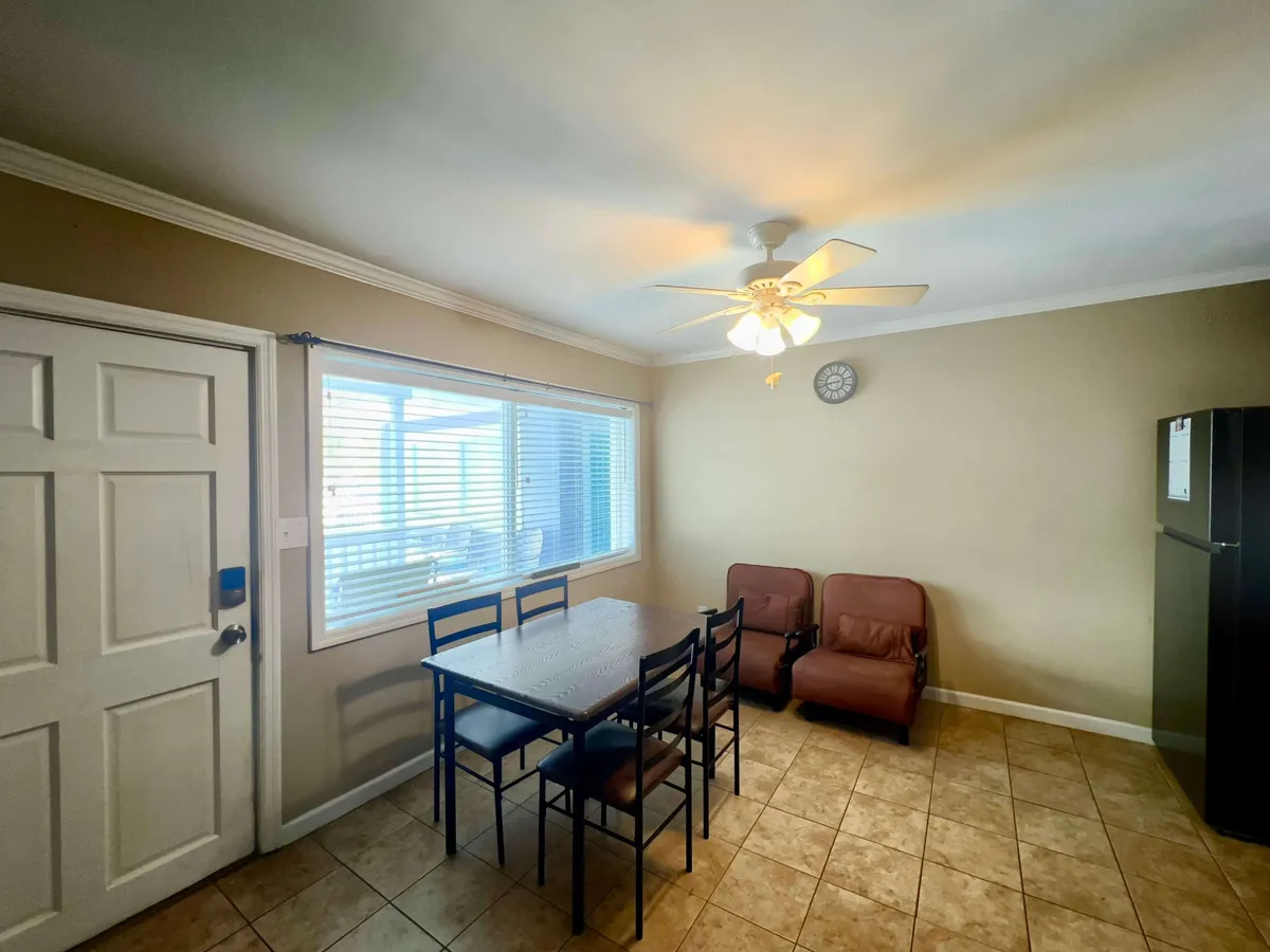 A cozy dining area with a table and chairs sits beside a sunlit window, with a ceiling fan and refrigerator nearby. The space feels warm and inviting—ideal for shared group meals or casual hangouts after a day of exploration.