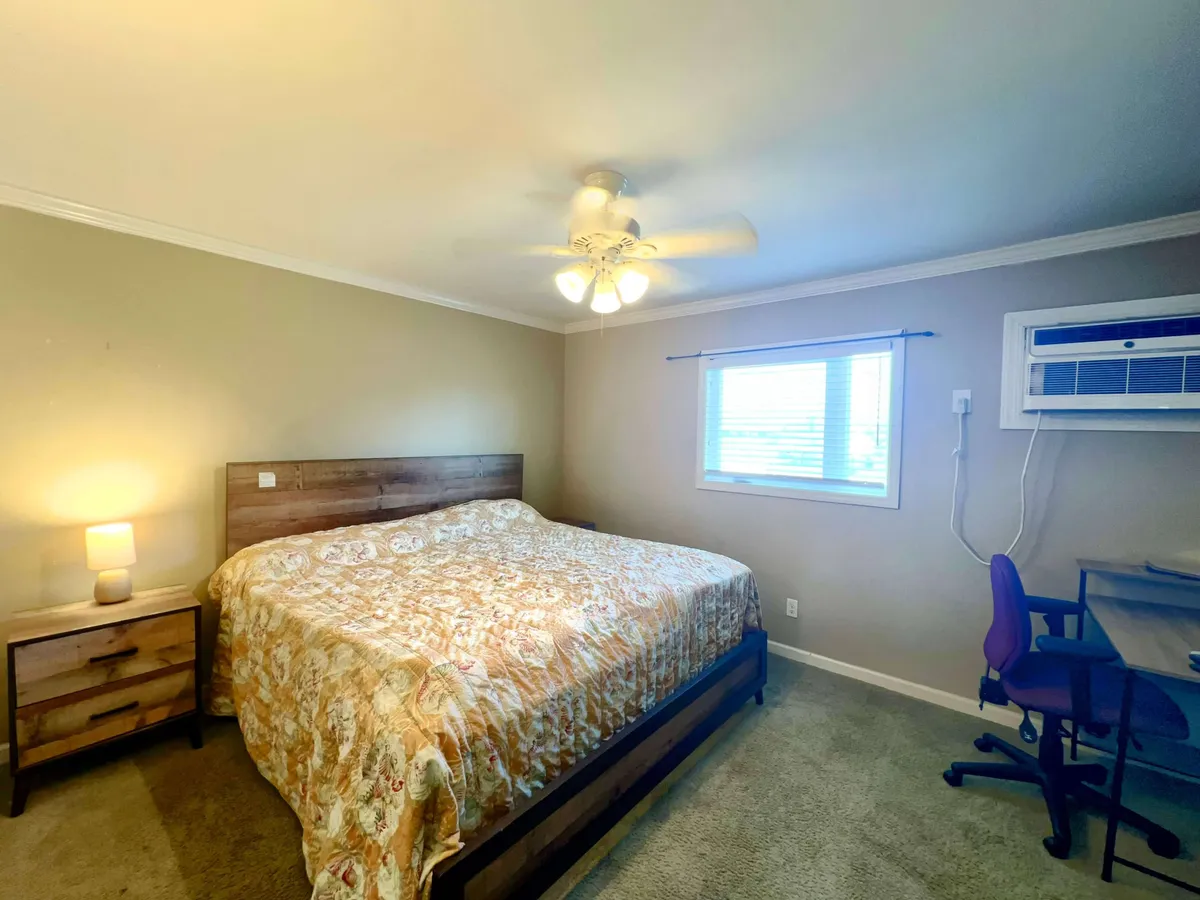 A serene bedroom featuring a comfortable bed, nightstand, window, and a small desk. The atmosphere is peaceful and well-appointed, blending areas for sleeping and quiet work or reading.