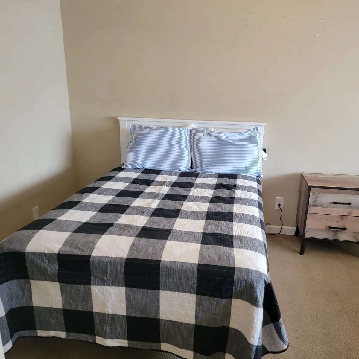A warmly lit bedroom featuring a bed with a black and white checkered quilt, complemented by blue striped pillows and a wooden nightstand. Subtle decorative touches and soft lighting create a cozy, inviting atmosphere ideal for relaxation after a day at the beach.