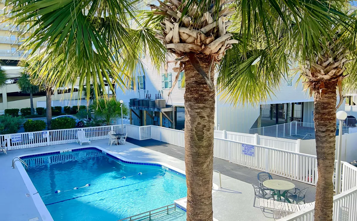 The hero image showcases a sparkling swimming pool surrounded by lush palm trees and inviting outdoor seating, all set against the backdrop of a leisurely North Myrtle Beach sunset. The scene captures the promise of both lively social gatherings by the pool and peaceful moments of relaxation.