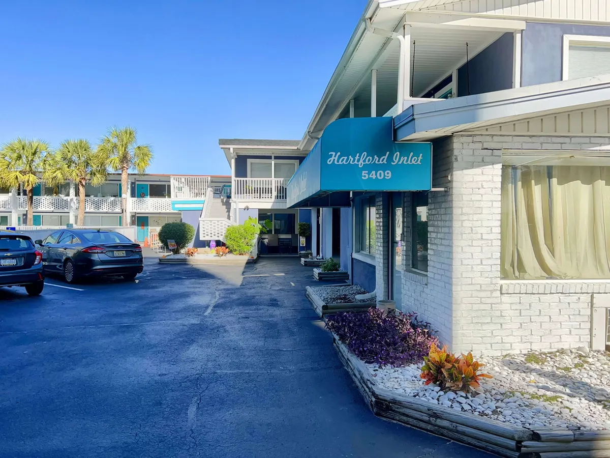 The exterior of Hartford Inlet is framed by palm trees and vibrant flowers under a cheerful sky. The welcoming sign and greenery create an inviting atmosphere and suggest proximity to local attractions and the beach.